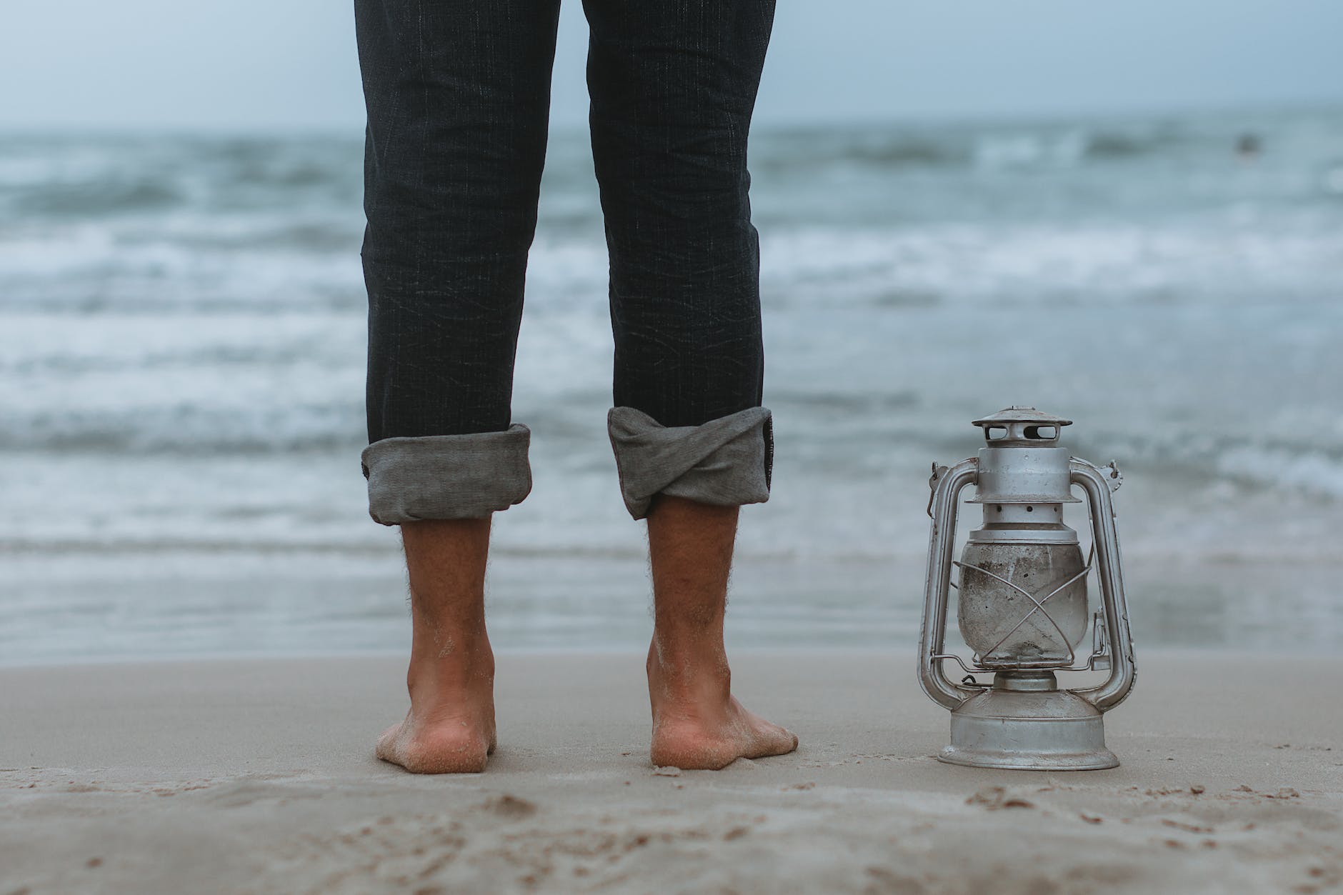 person standing on shoreline beside gray tubular lantern